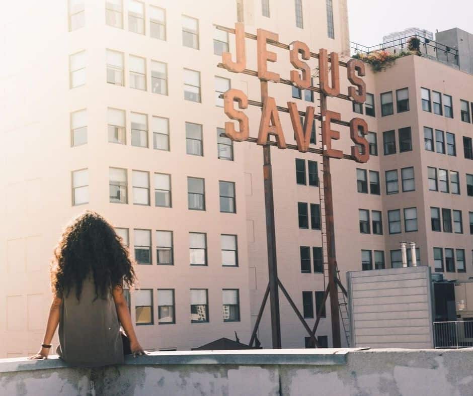 woman sitting in front of a sign that says "Jesus Saves"